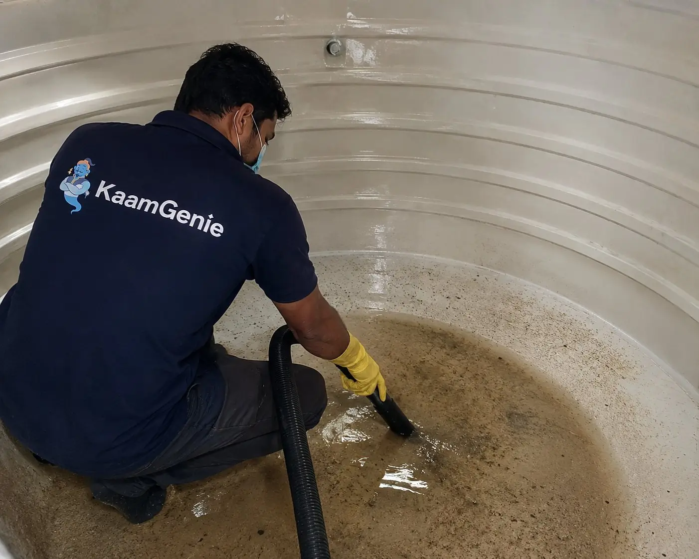 KaamGenie crew member inside a plastic water tank using a wet vacuum to suction out dirty residual water and dislodged sediment