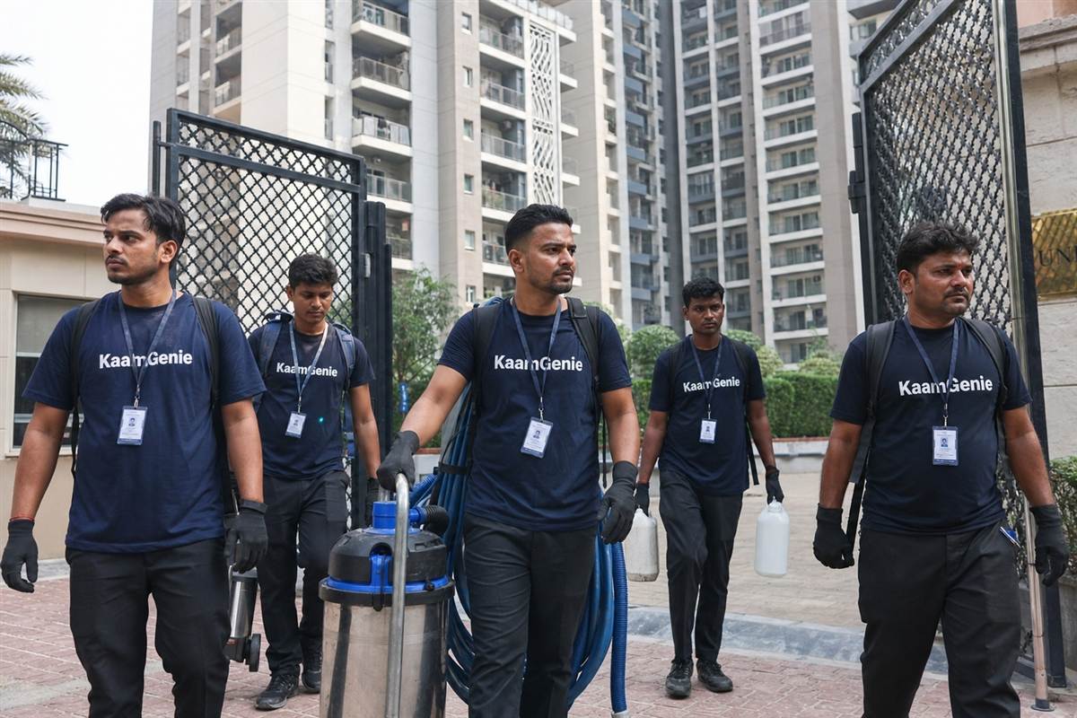 KaamGenie technician in a navy-blue branded shirt hand-scooping dark sludge from the bottom of a drained Gurgaon water tank into a sealed bucket