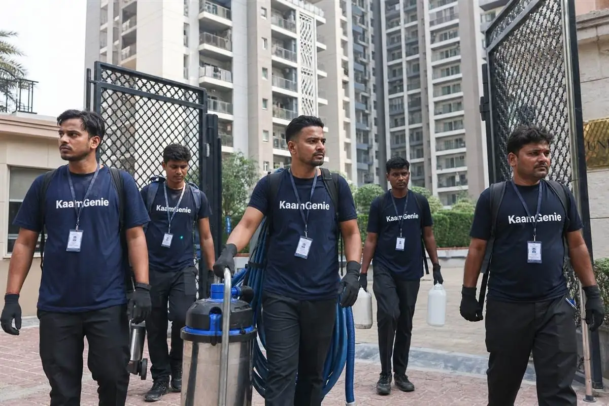 KaamGenie technician in a navy-blue branded shirt hand-scooping dark sludge from the bottom of a drained Gurgaon water tank into a sealed bucket