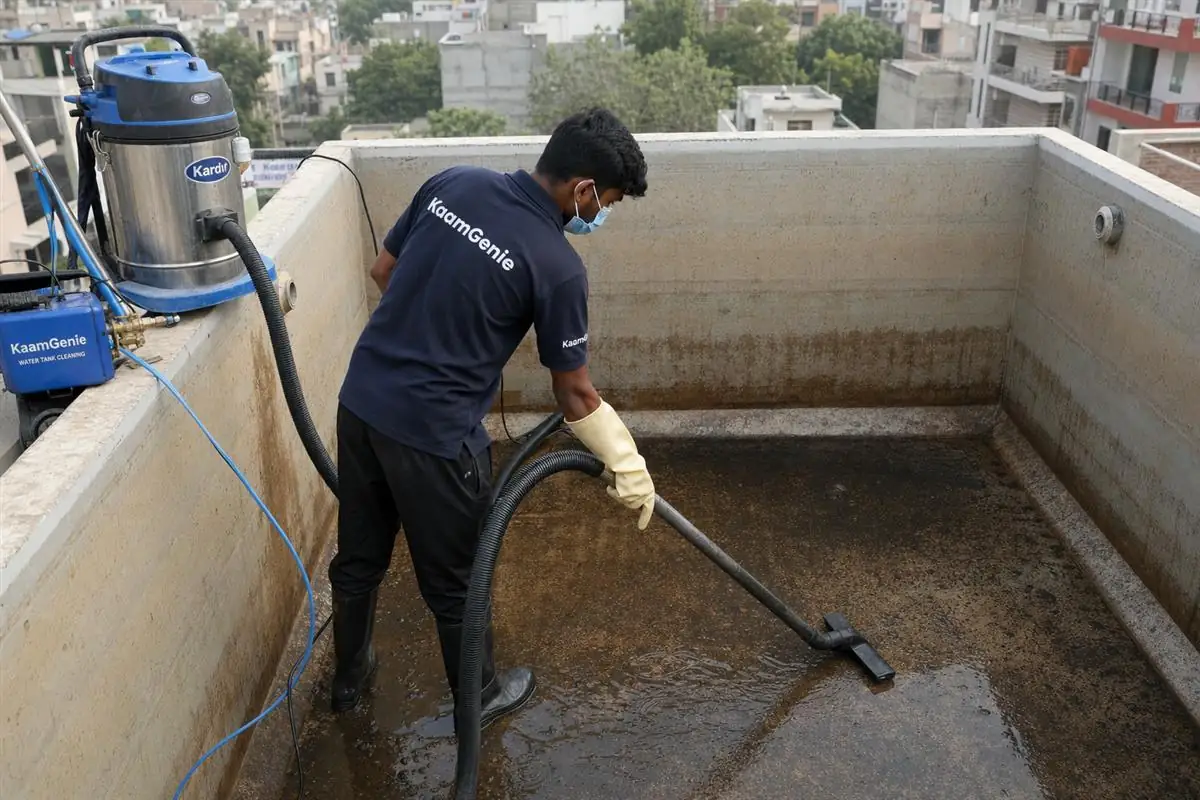 KaamGenie technician in navy uniform vacuuming dark sludge from the floor of a drained overhead water tank in Delhi