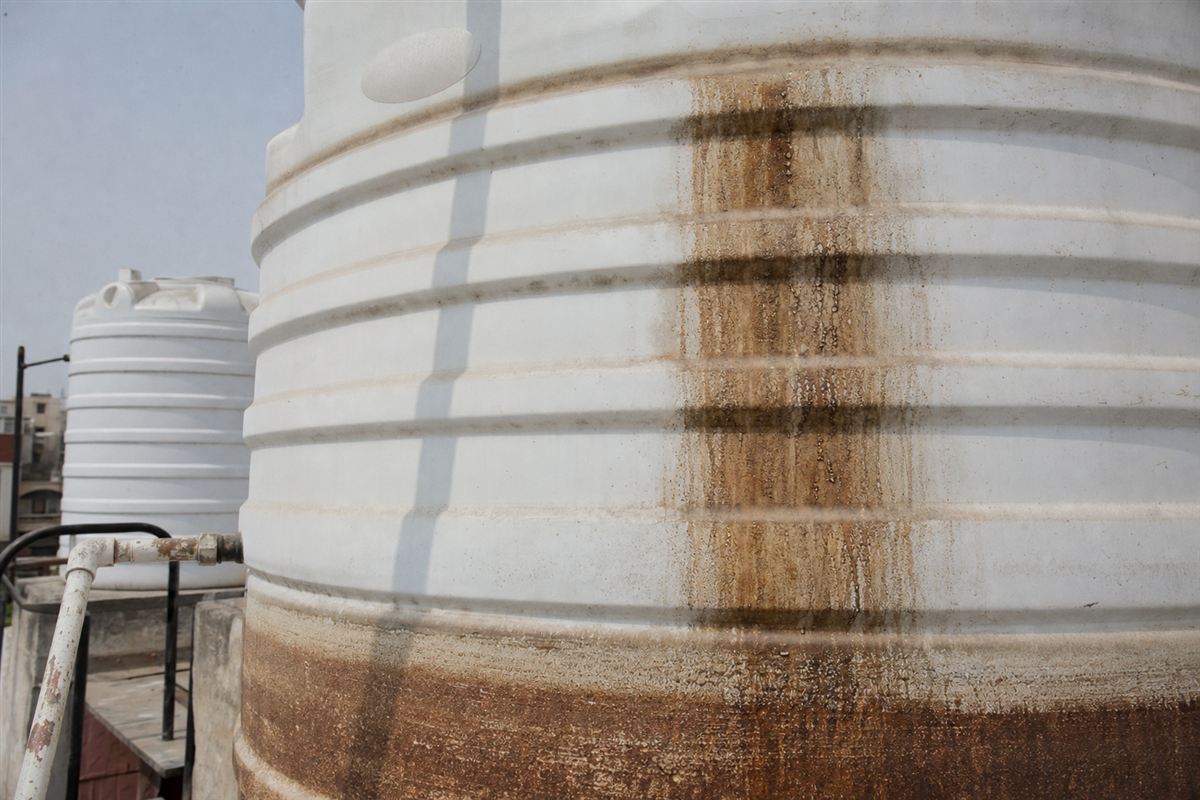 Close-up of reddish-brown iron staining and hard-water sediment crusted on the inside wall of a Gurgaon borewell tank