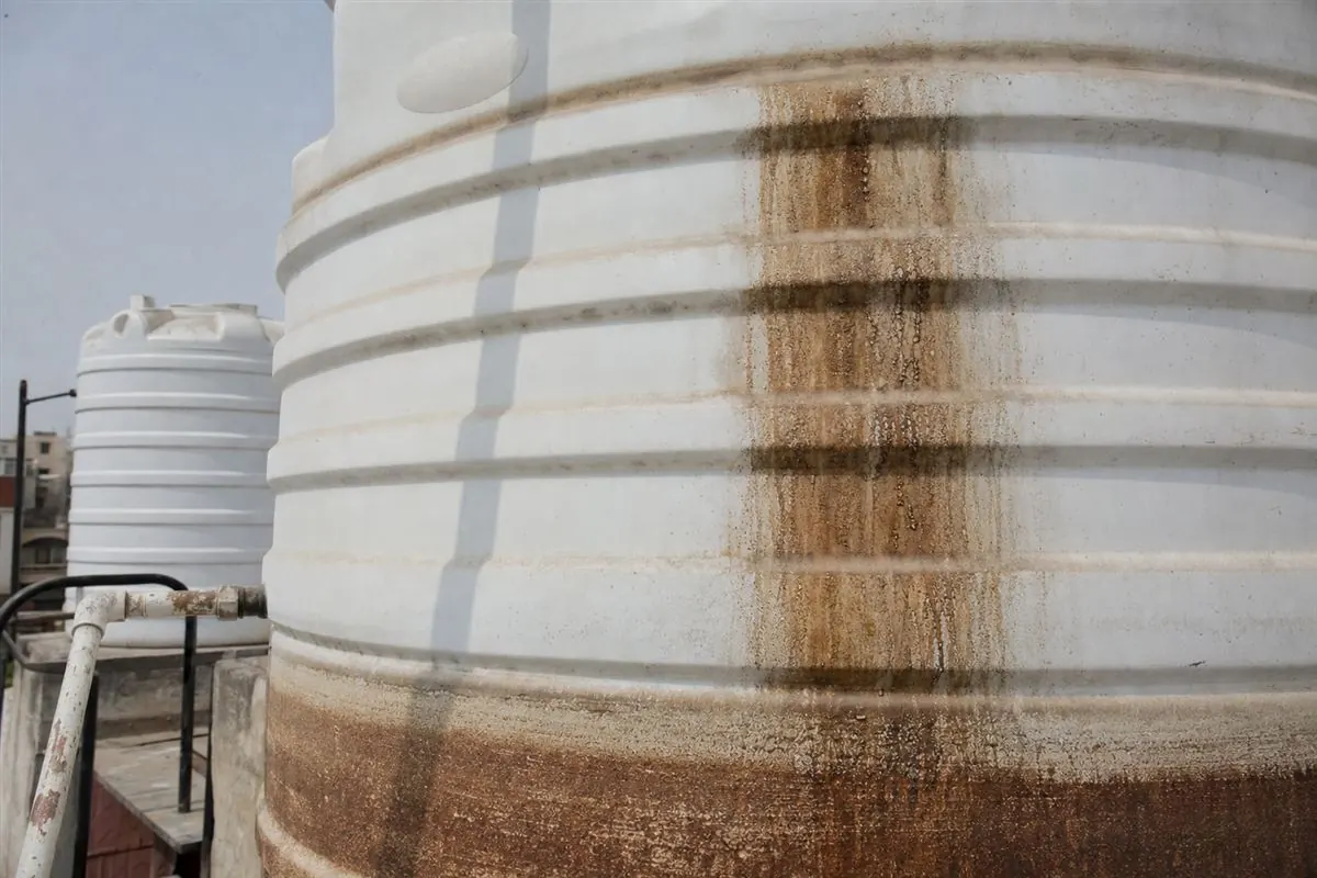 Close-up of reddish-brown iron staining and hard-water sediment crusted on the inside wall of a Gurgaon borewell tank