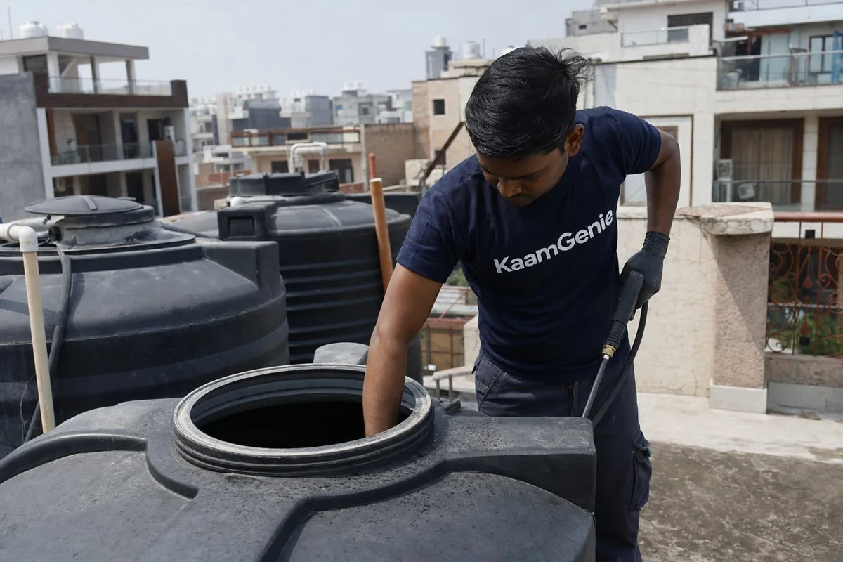 KaamGenie crew cleaning rooftop water tanks on an independent builder floor terrace in Gurgaon, with a low-rise DLF colony behind