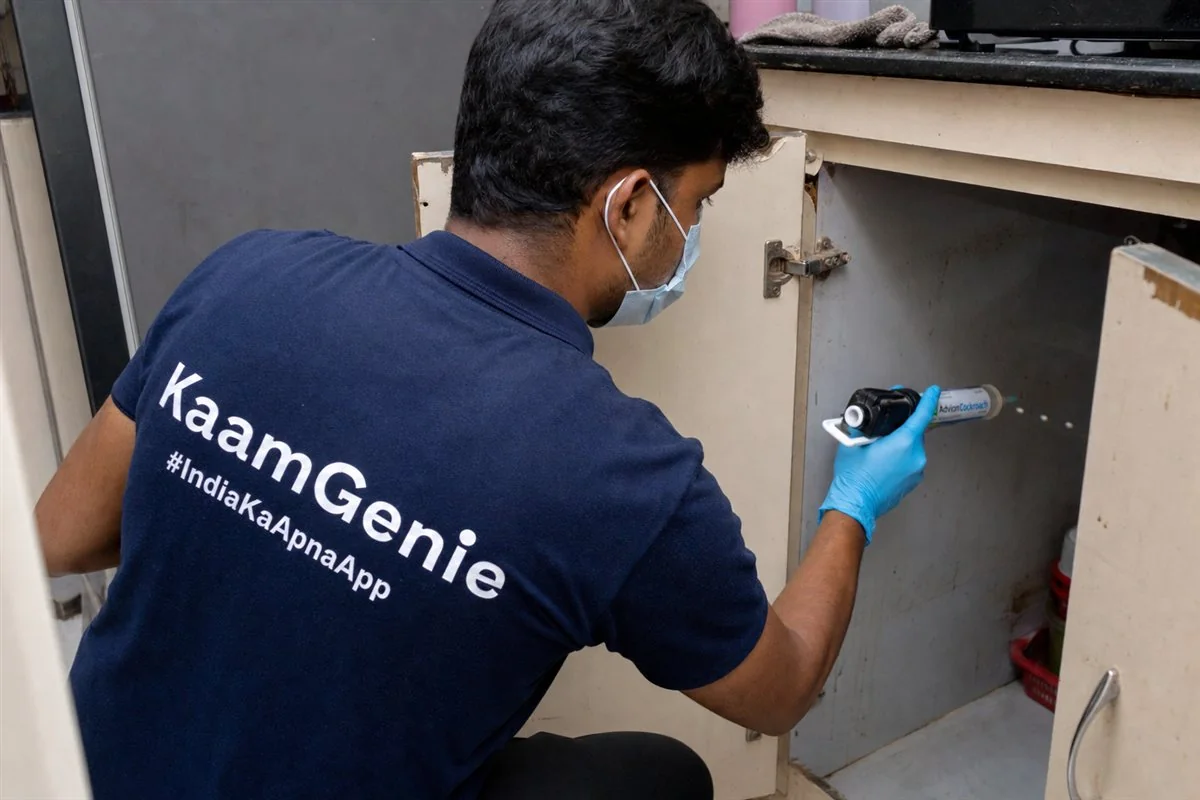 KaamGenie technician applying odourless cockroach gel bait along a Delhi kitchen cabinet hinge with a precision applicator
