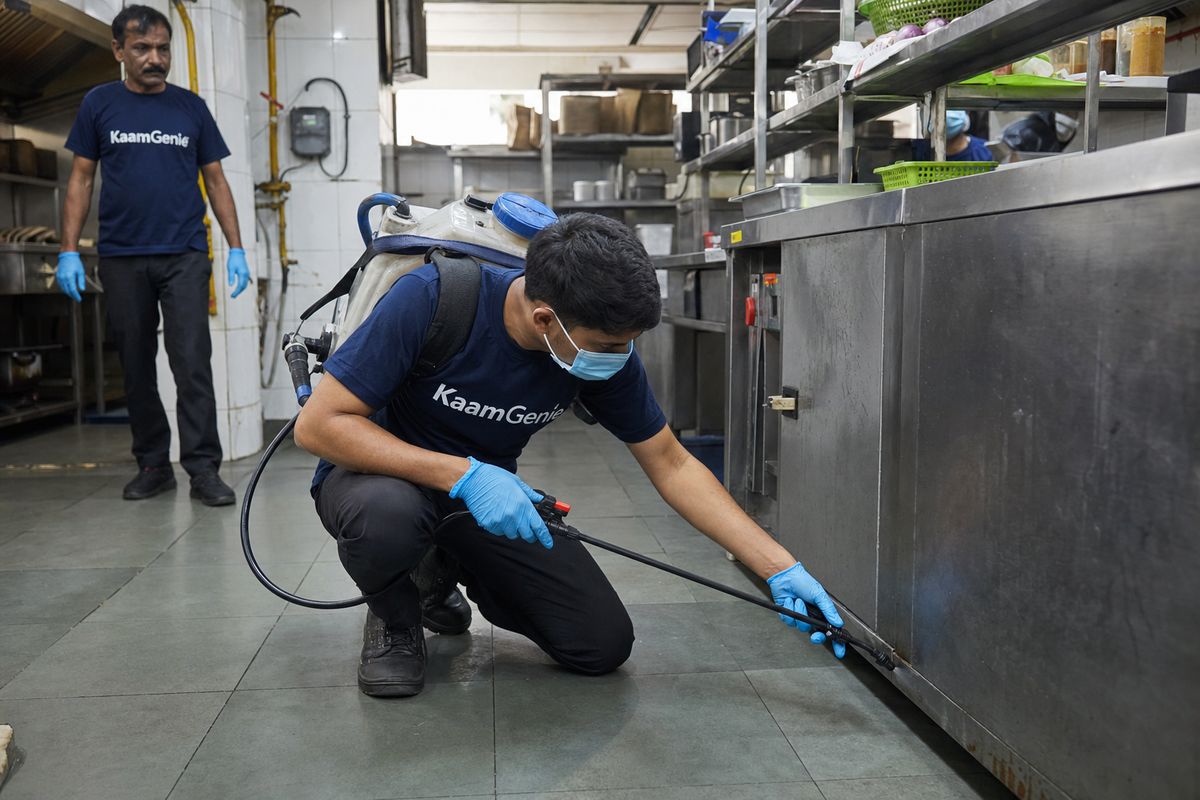KaamGenie technician applying low-odour spray treatment along stainless steel kitchen prep tables in a Delhi restaurant