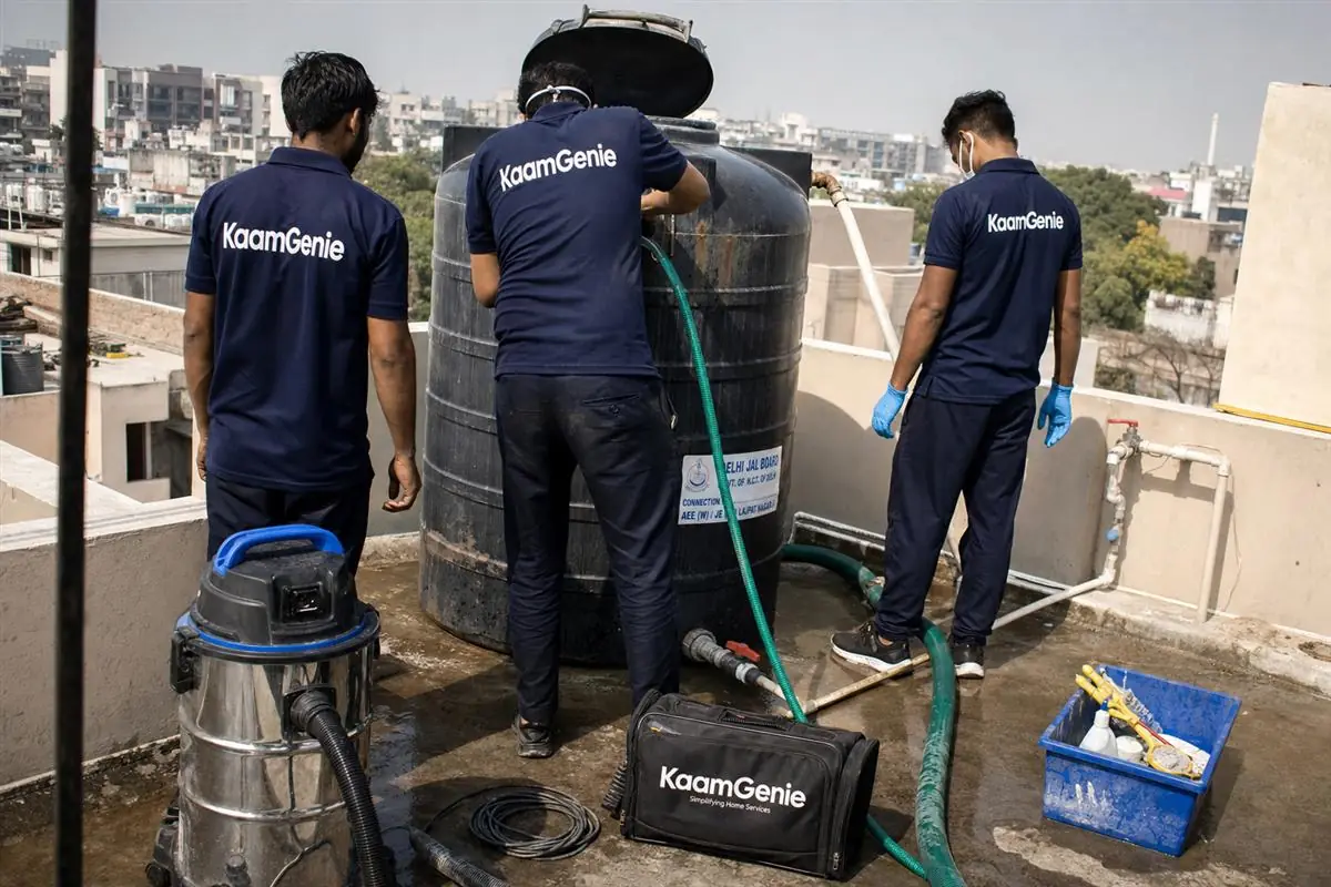 KaamGenie crew in navy uniforms inspecting an overhead water tank fed by a Delhi Jal Board connection on a Delhi rooftop