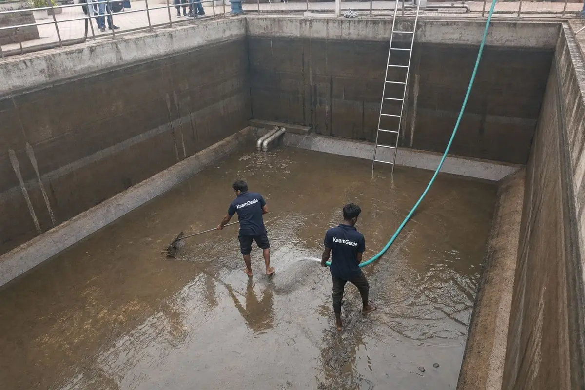 Two KaamGenie crew members in navy shirts cleaning a large society underground reservoir in a Dwarka tower basement