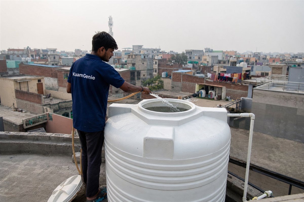 A KaamGenie crew member in a navy shirt rinsing a clean Dwarka tower rooftop tank with a hose after disinfection