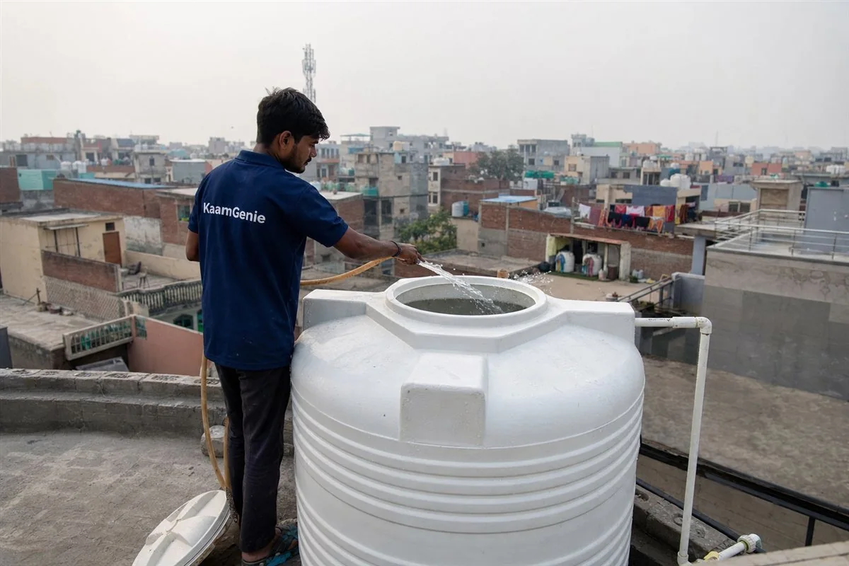 A KaamGenie crew member in a navy shirt rinsing a clean Dwarka tower rooftop tank with a hose after disinfection