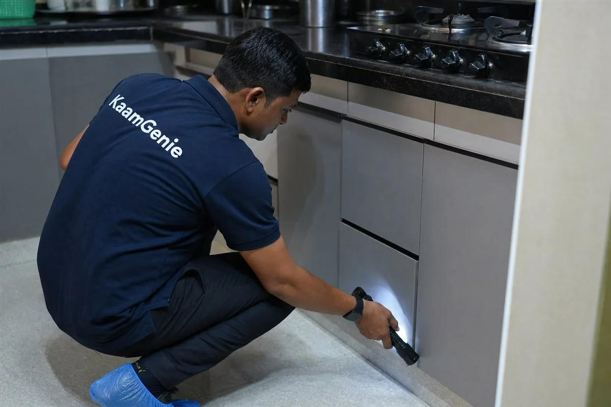 A KaamGenie rodent control technician inspecting under a Delhi kitchen unit during an emergency rat callout