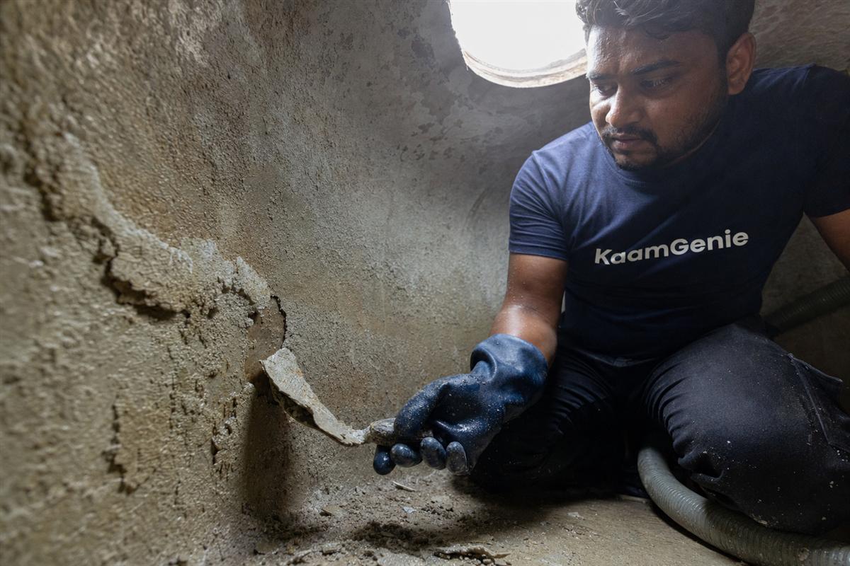KaamGenie crew scraping thick chalky white calcium scale off the inside wall of an overhead water tank in Gurgaon