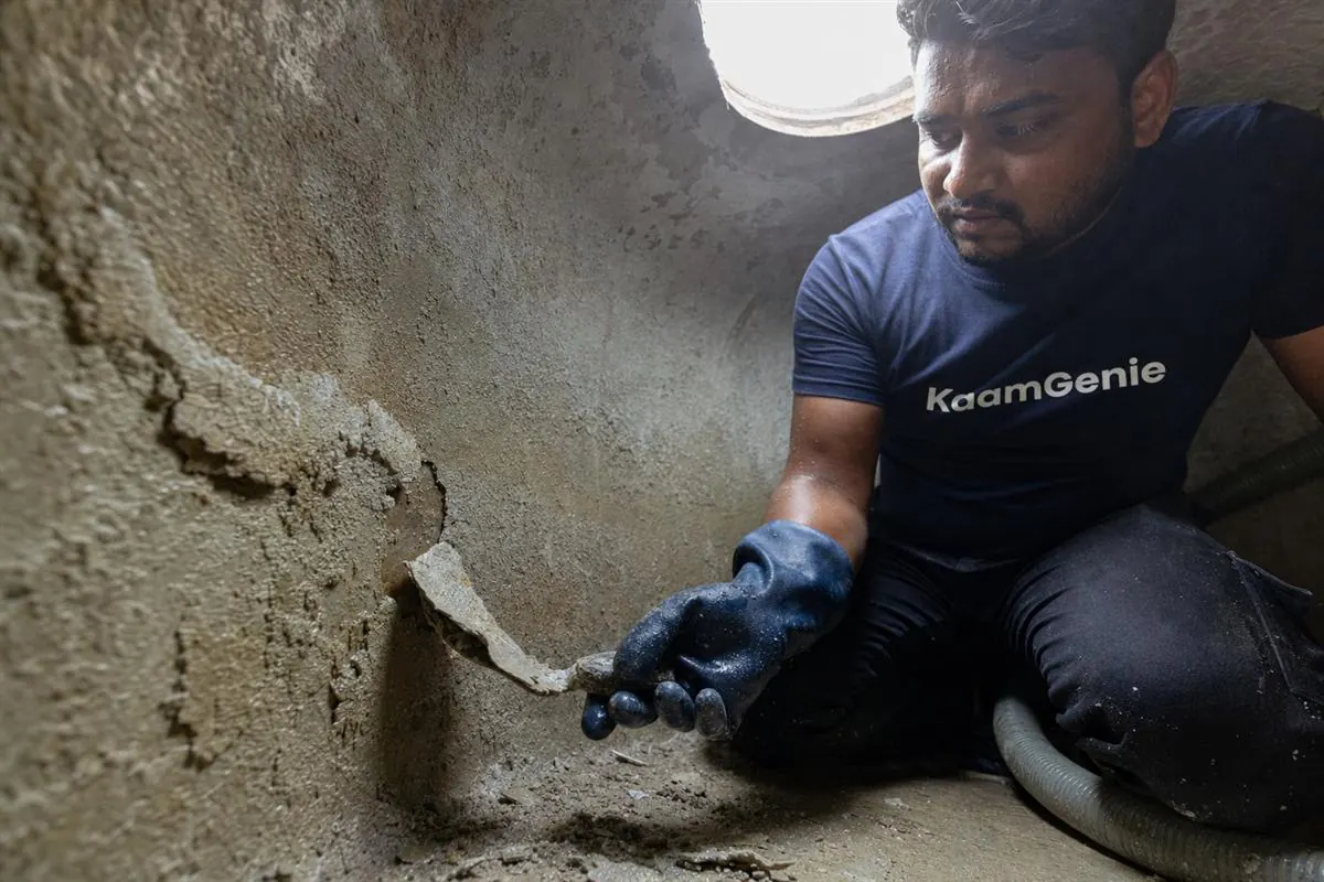 KaamGenie crew scraping thick chalky white calcium scale off the inside wall of an overhead water tank in Gurgaon