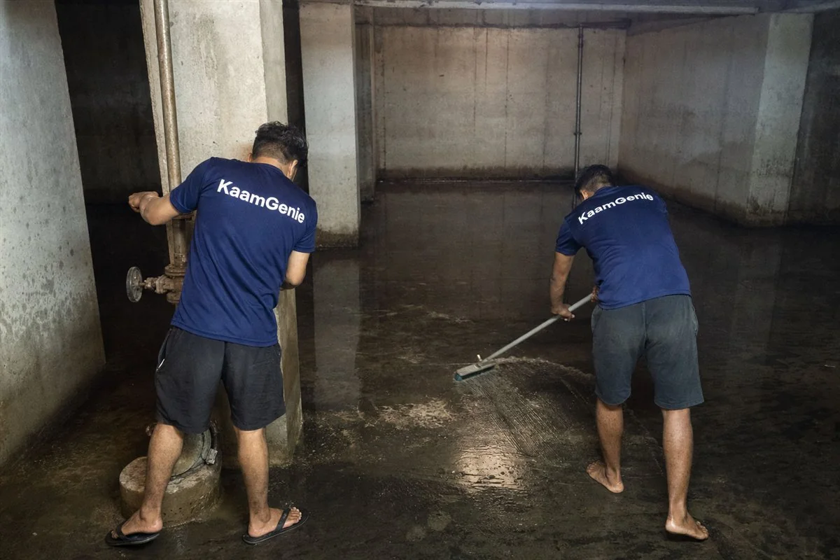 Two KaamGenie workers in navy shirts cleaning a large high-rise underground reservoir in Gurgaon