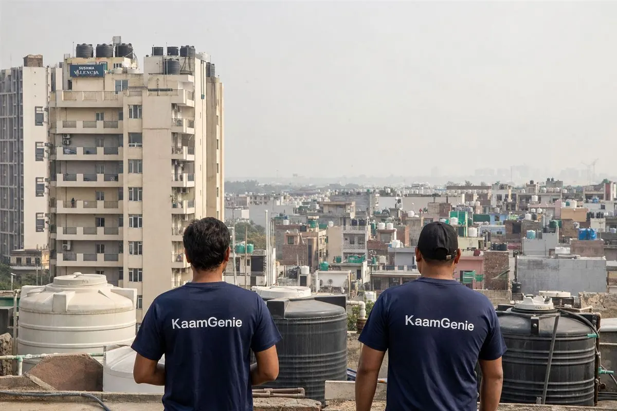 Split scene - a tall Dwarka society tower with rooftop overhead tanks on one side and low plotted Delhi homes on the other