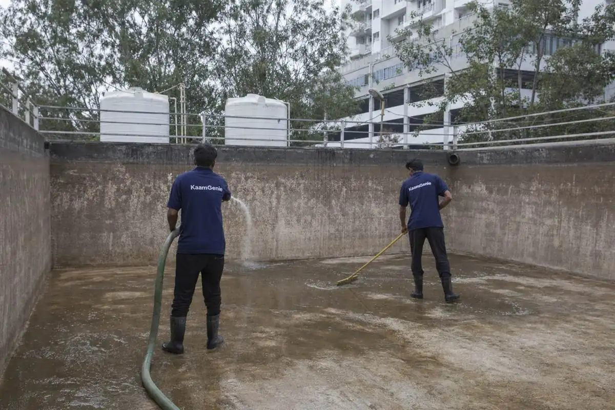 Two KaamGenie workers in navy shirts cleaning a huge underground concrete reservoir at a Gurgaon high-rise society
