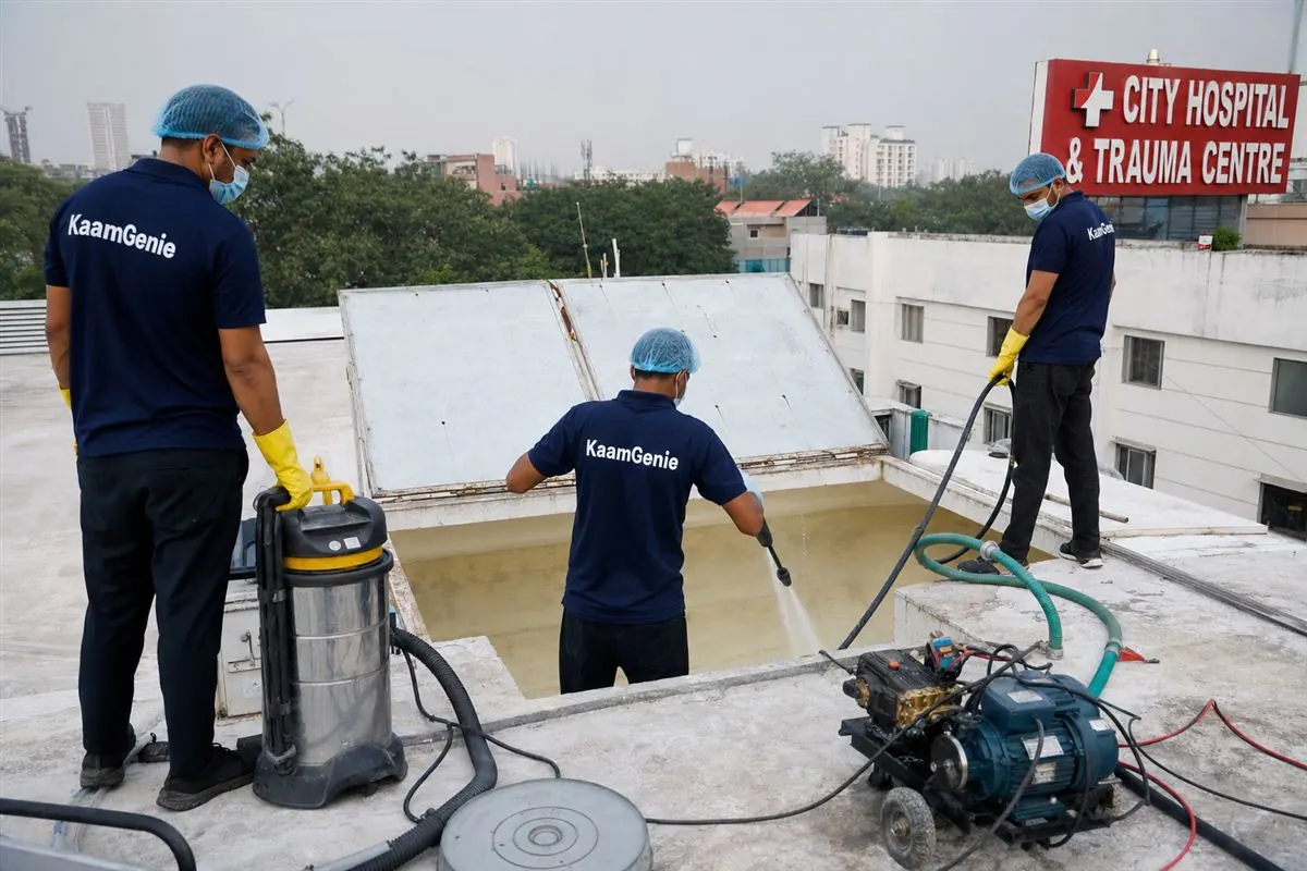 KaamGenie technicians in navy uniforms disinfecting a large overhead water tank on a Delhi hospital rooftop