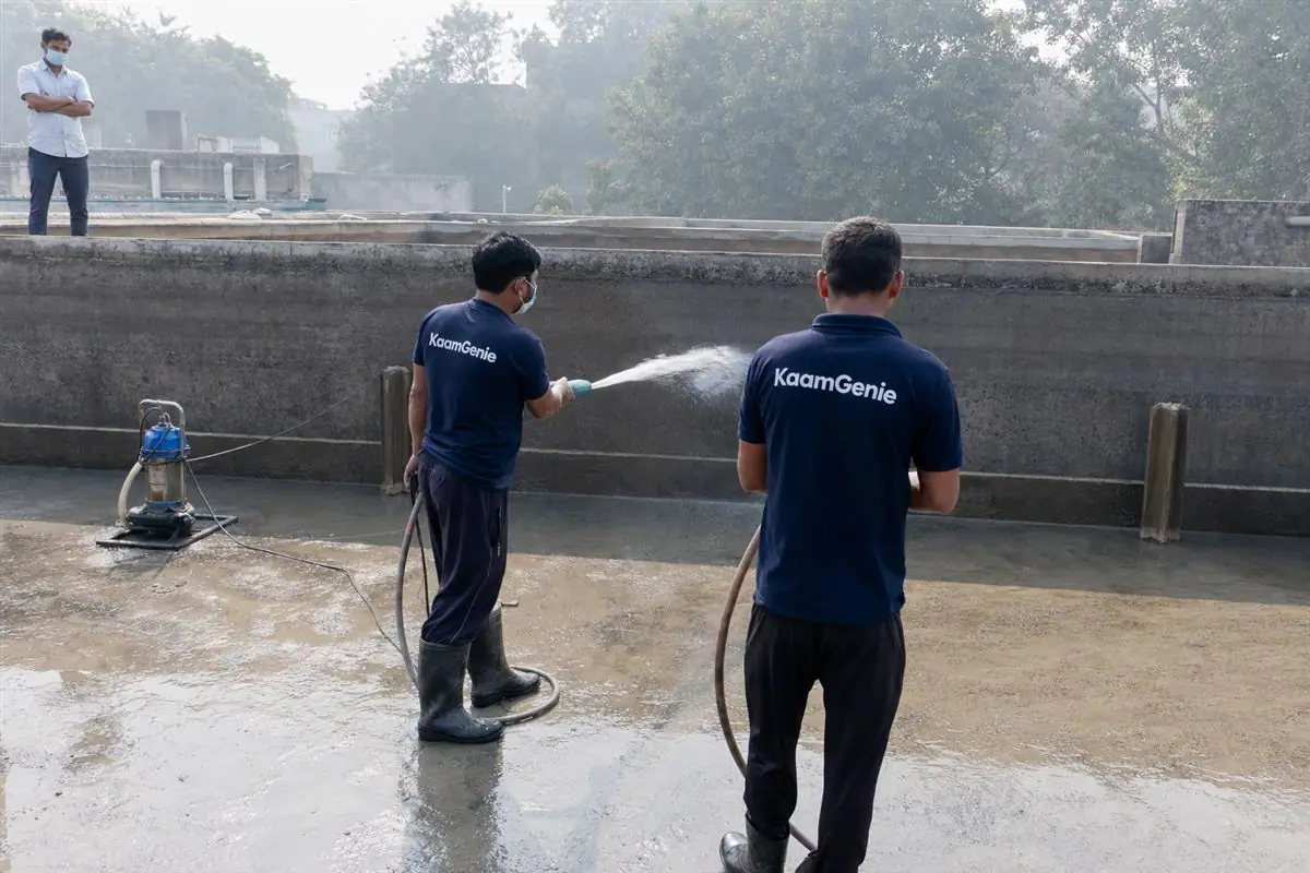 Two KaamGenie workers in navy shirts cleaning a very large underground reservoir at a Gurgaon hospital campus