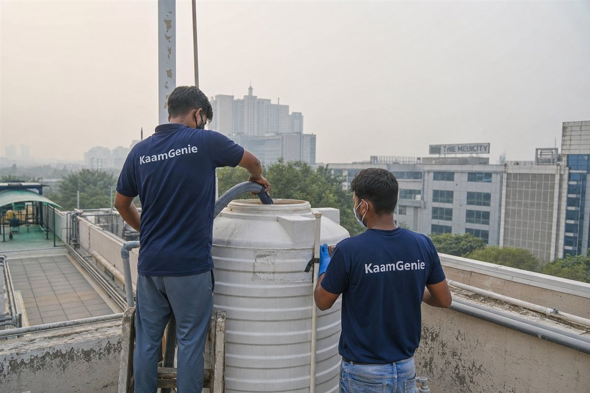Two KaamGenie workers in navy shirts disinfecting a rooftop tank at a Gurgaon healthcare facility