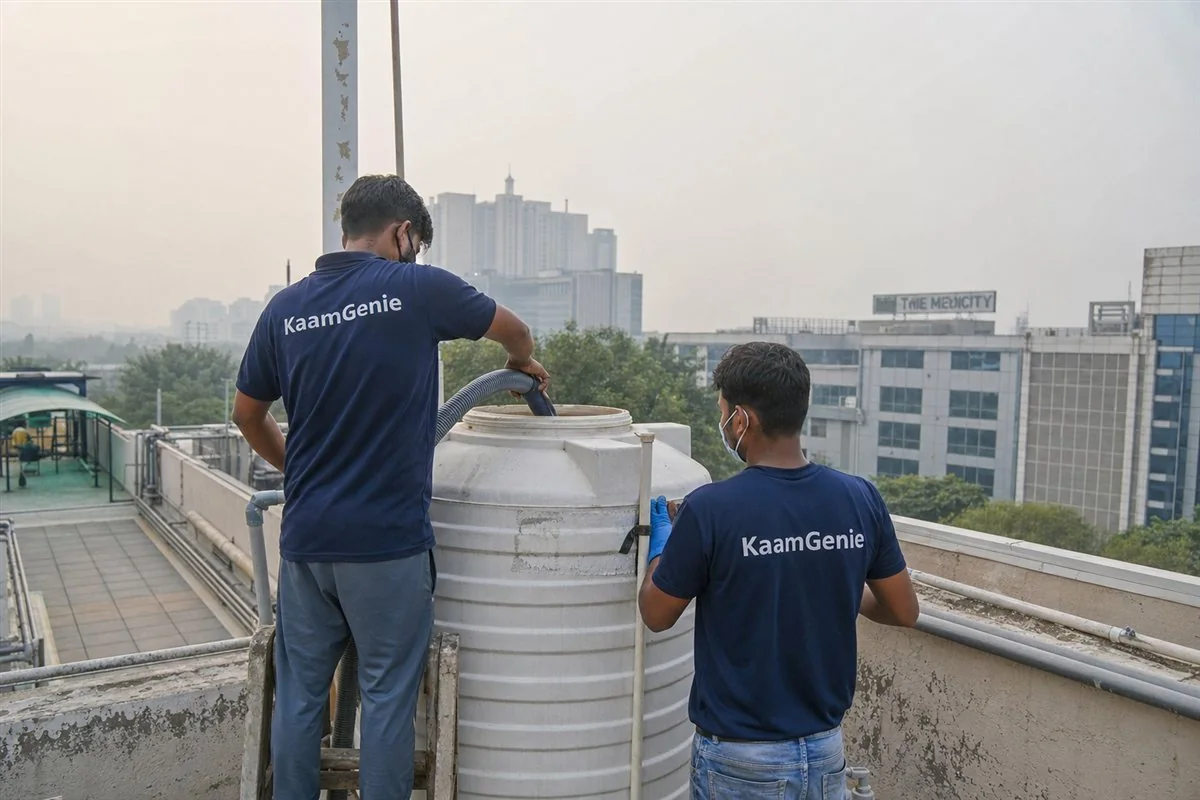 Two KaamGenie workers in navy shirts disinfecting a rooftop tank at a Gurgaon healthcare facility