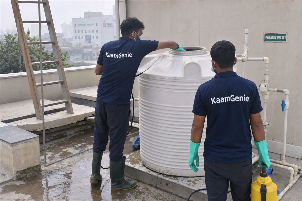 Two KaamGenie workers in navy shirts disinfecting a rooftop tank at a Noida healthcare facility