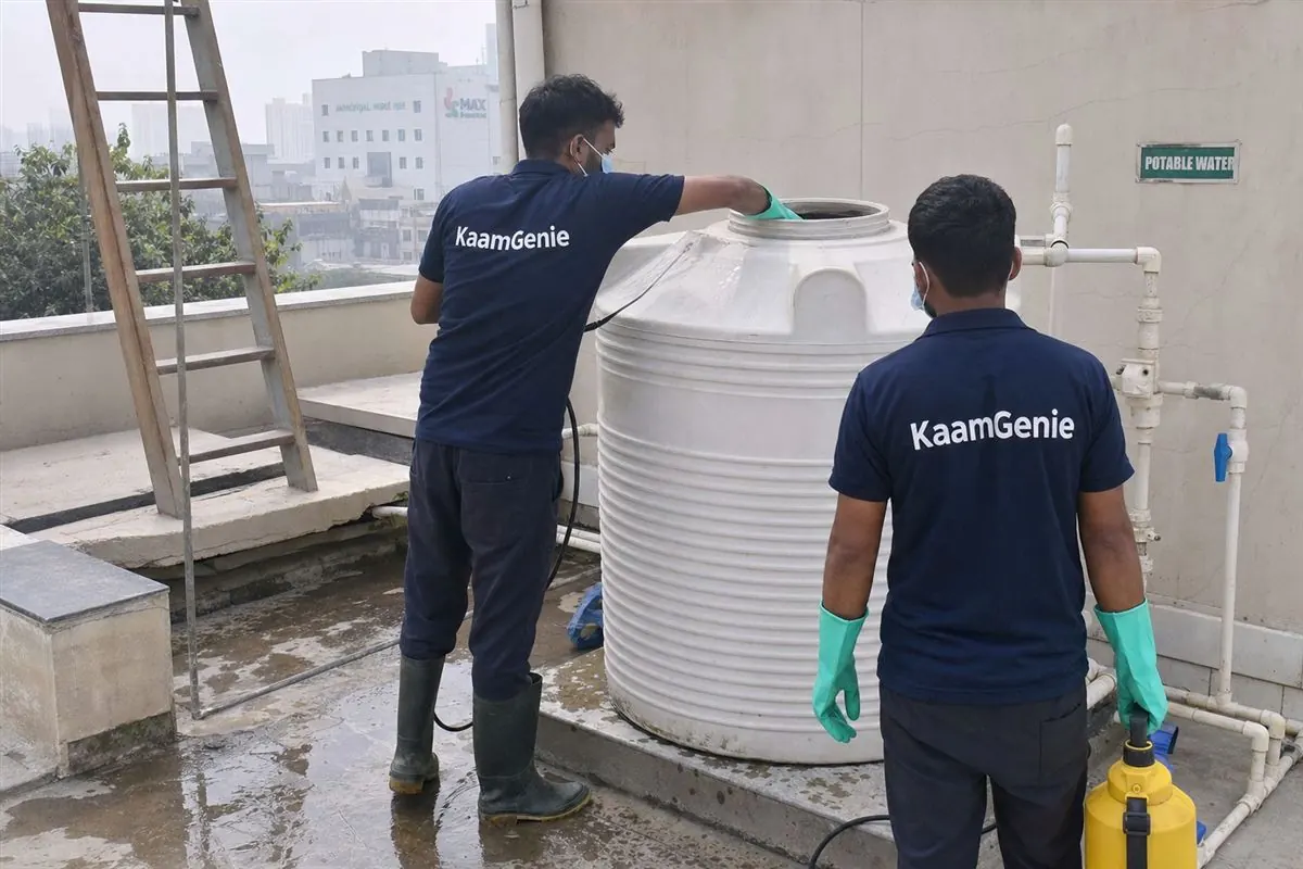 Two KaamGenie workers in navy shirts disinfecting a rooftop tank at a Noida healthcare facility