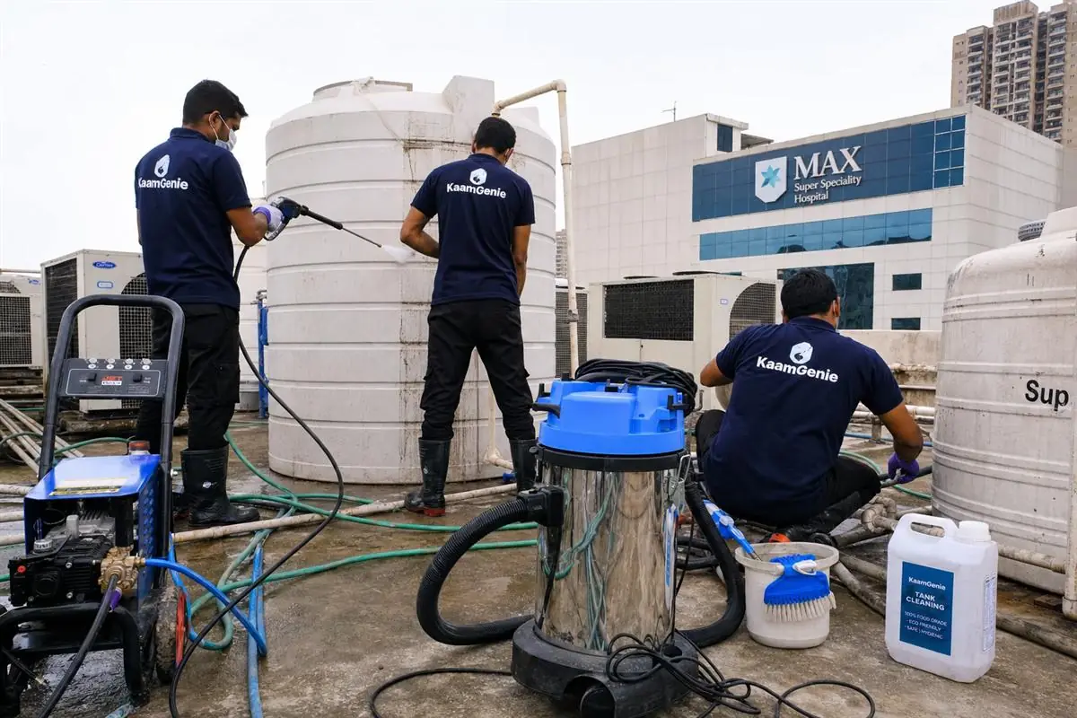 KaamGenie crew in navy uniforms servicing a large water storage tank on the terrace of a Delhi hospital building