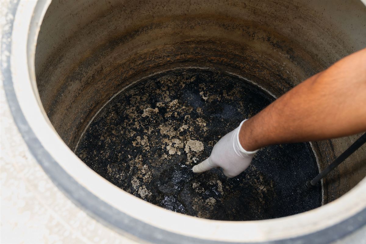 Close-up of thick black sludge and hard-water scale at the bottom of a neglected Delhi water tank, showing why a heavily soiled tank takes longer to clean