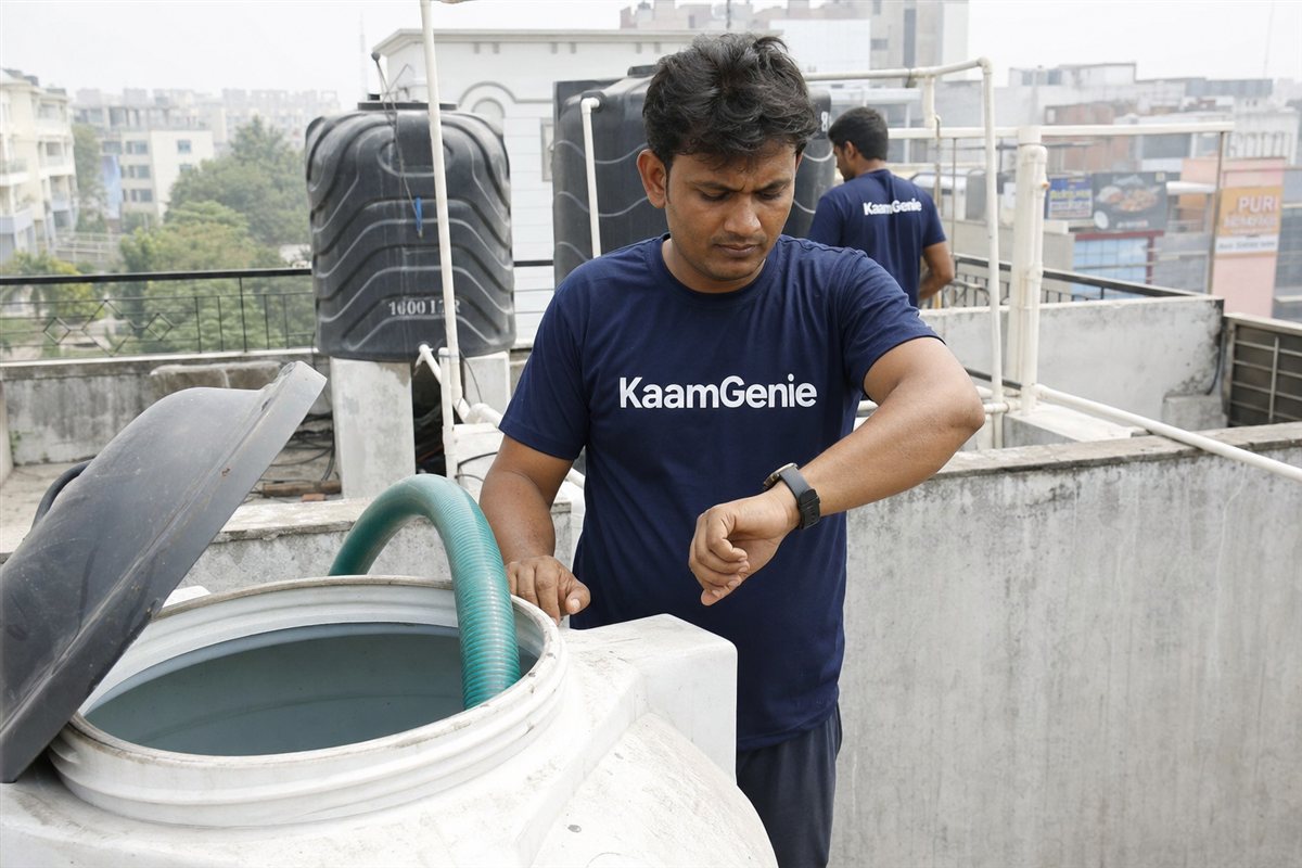 KaamGenie worker in a navy shirt checking the time while cleaning a rooftop water tank on a Gurgaon terrace