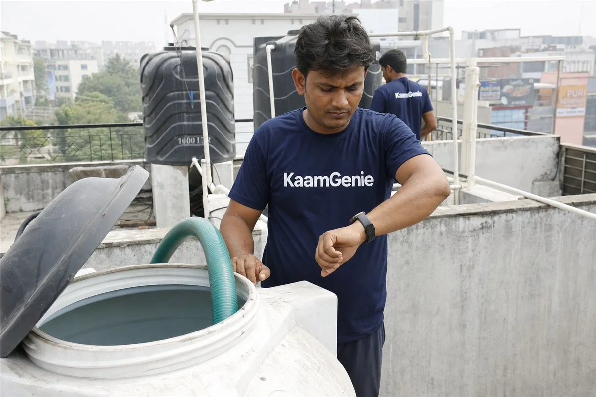 KaamGenie worker in a navy shirt checking the time while cleaning a rooftop water tank on a Gurgaon terrace