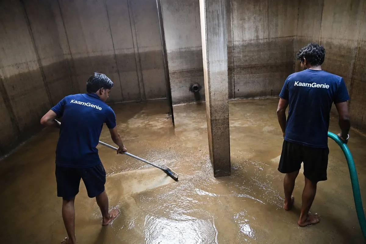 Two KaamGenie workers in navy shirts cleaning a large underground reservoir at a Gurgaon high-rise
