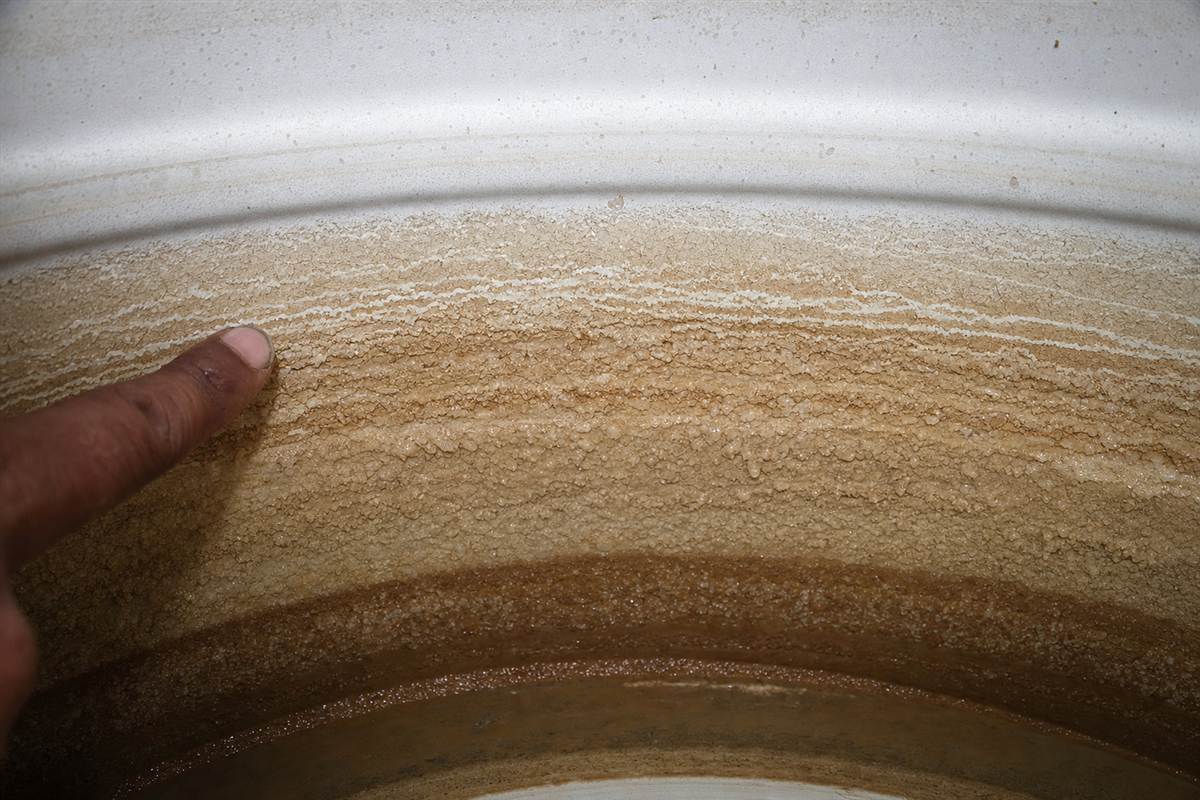 Thick white calcium scale and grey sediment on the inside floor of a Gurgaon overhead tank fed by hard borewell water