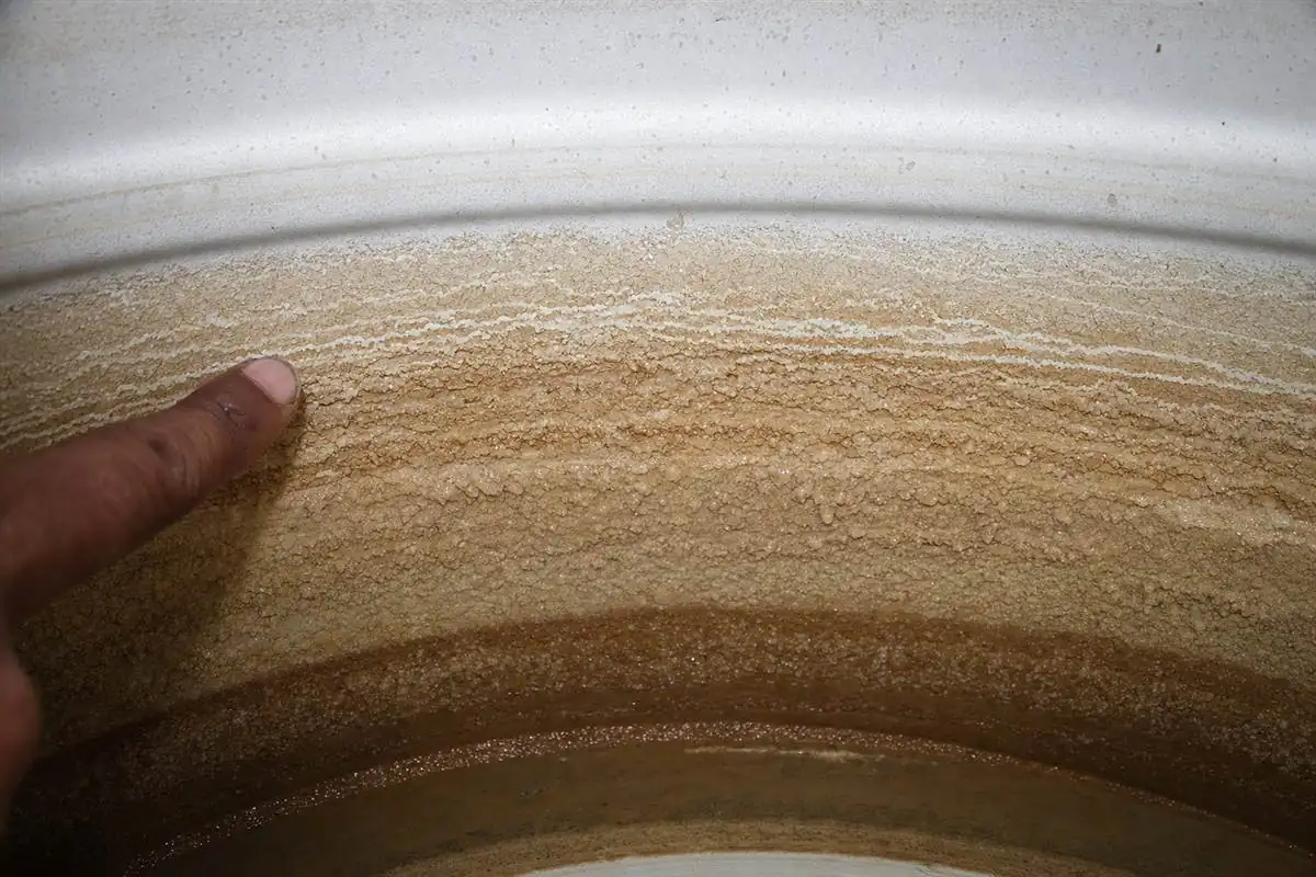 Thick white calcium scale and grey sediment on the inside floor of a Gurgaon overhead tank fed by hard borewell water