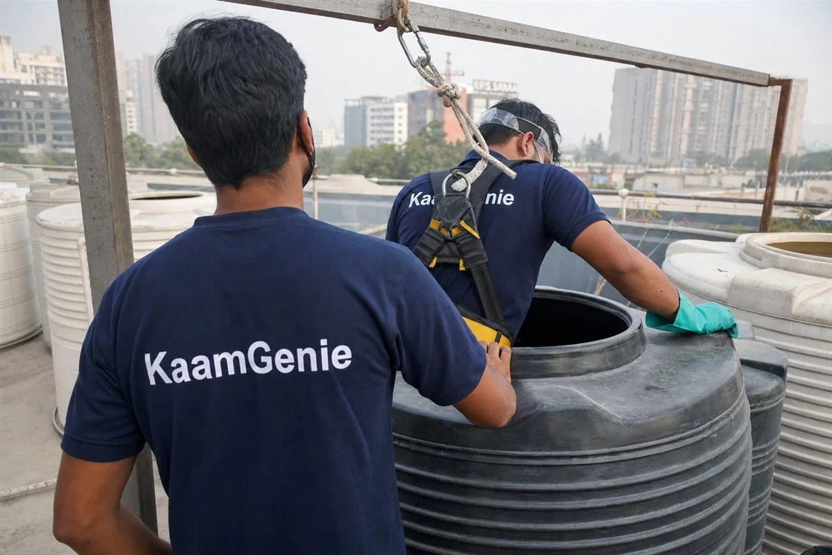 A KaamGenie worker in a navy shirt safely entering a large water tank with a harness, gas meter and proper confined-space equipment