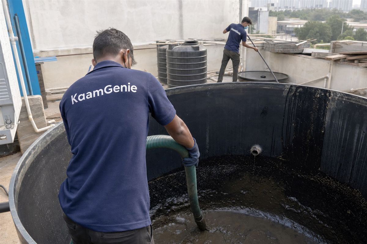 KaamGenie worker in a navy shirt vacuuming heavy sediment from the floor of a large industrial water storage tank in Gurgaon