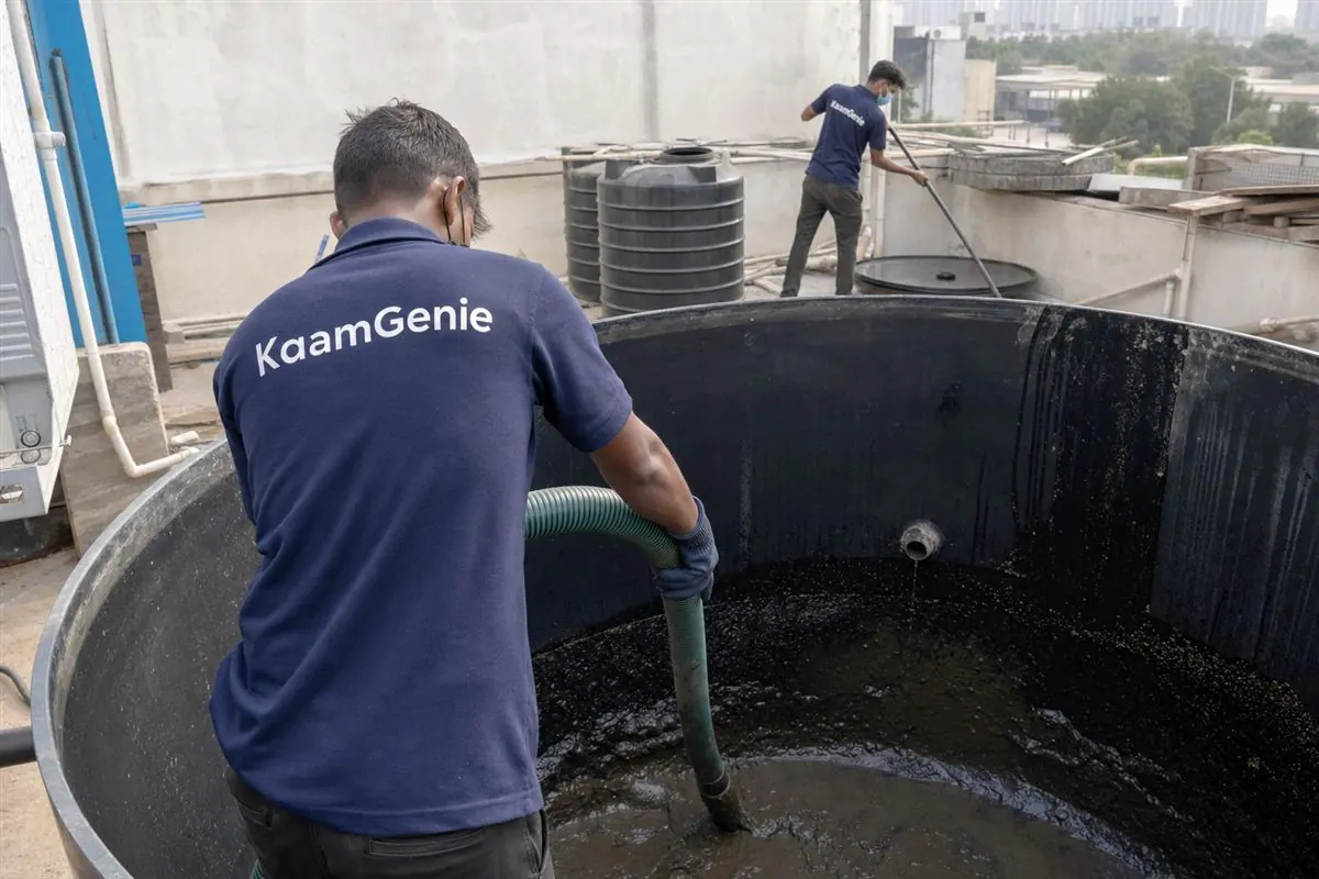KaamGenie worker in a navy shirt vacuuming heavy sediment from the floor of a large industrial water storage tank in Gurgaon