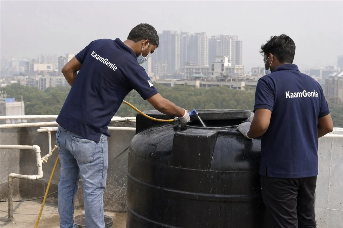 Two KaamGenie crew members disinfecting a large institutional rooftop water tank on a Noida campus