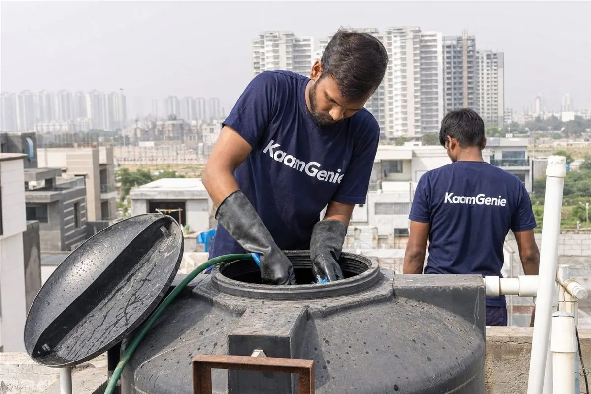 A KaamGenie worker in a navy shirt cleaning a rooftop water tank on a new building in the YEIDA airport belt