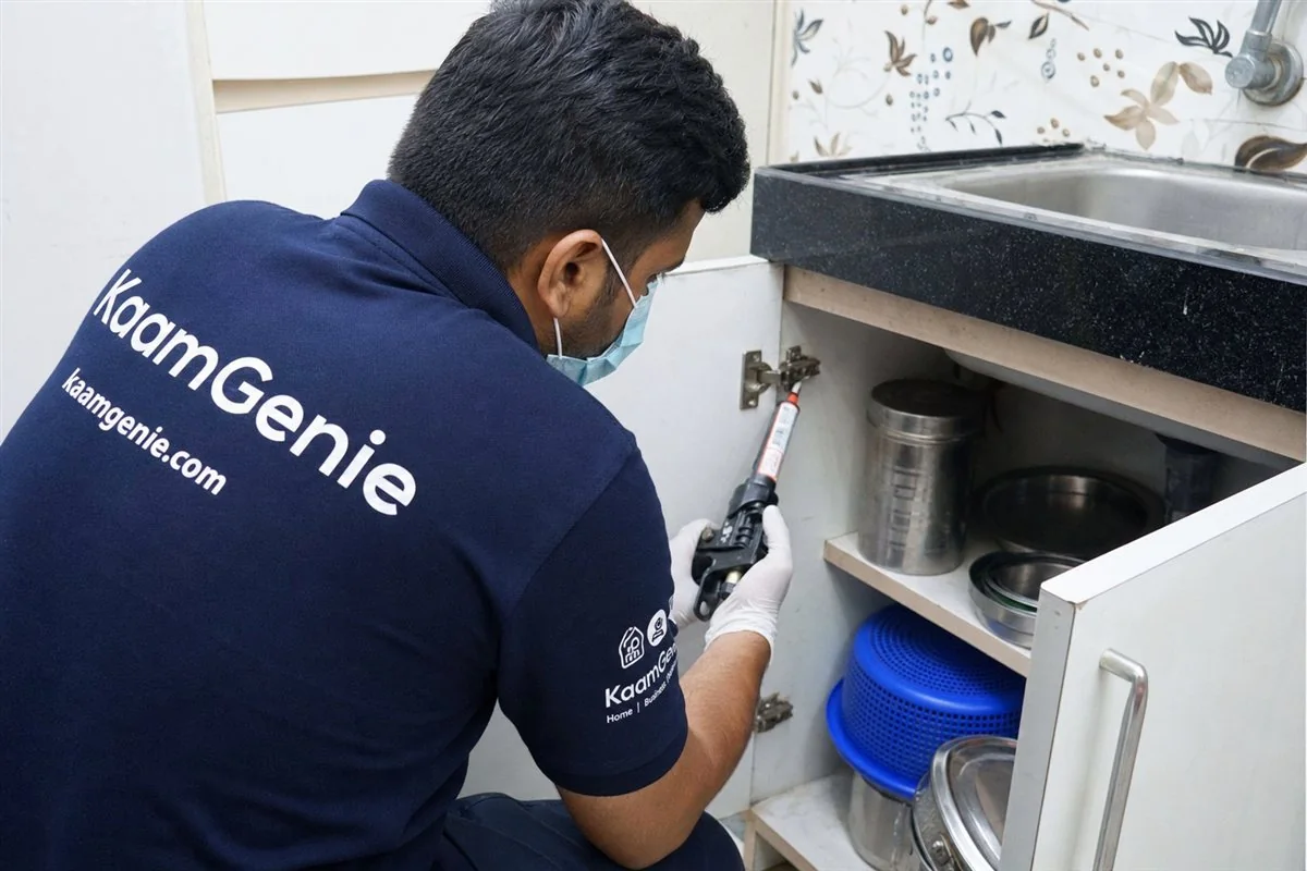KaamGenie technician applying odourless gel-bait along a Delhi kitchen cabinet hinge for food-safe cockroach control