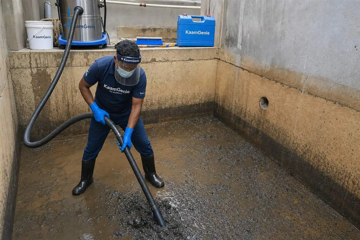 KaamGenie technician vacuuming thick brown silt and sediment from the floor of a drained underground water sump in Delhi