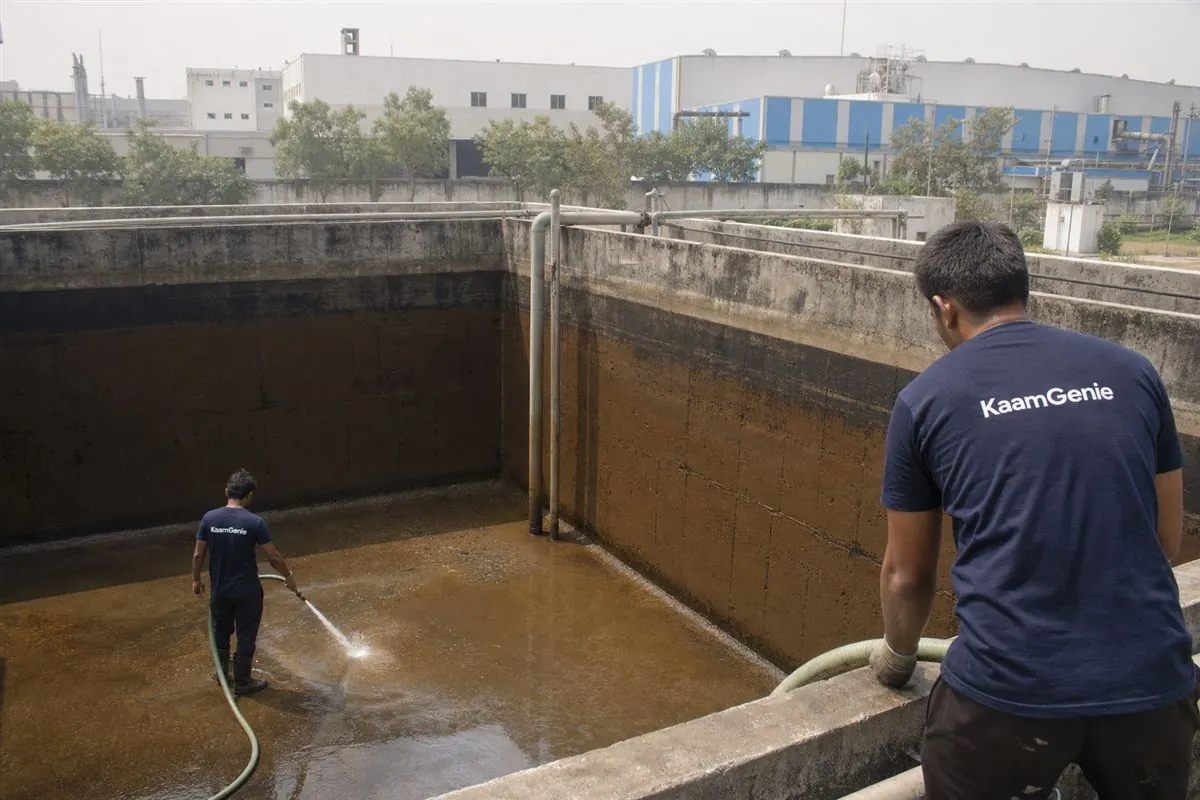 KaamGenie crew cleaning a large underground water reservoir at an IMT Manesar township in Gurgaon, with factory sheds in the background