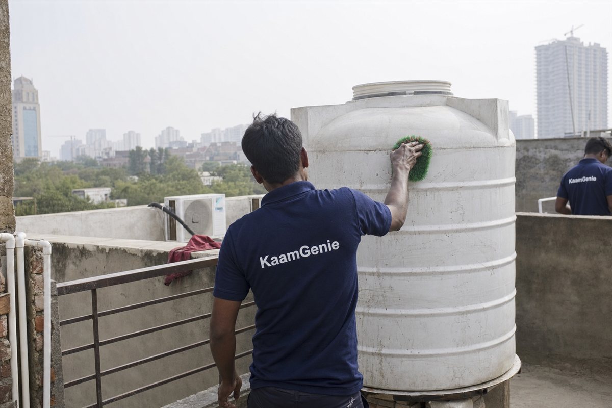 KaamGenie crew member in a navy shirt scrubbing the inside of a rooftop water tank on a worker-housing block in Manesar, Gurgaon