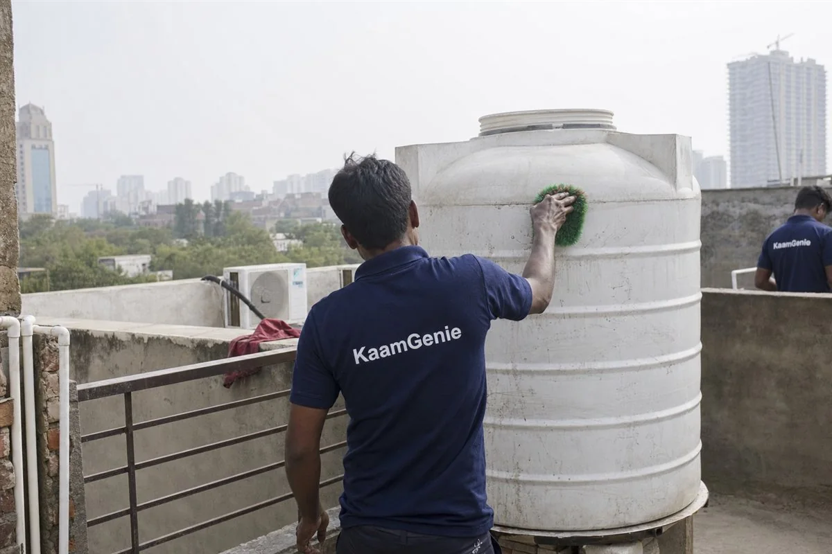 KaamGenie crew member in a navy shirt scrubbing the inside of a rooftop water tank on a worker-housing block in Manesar, Gurgaon