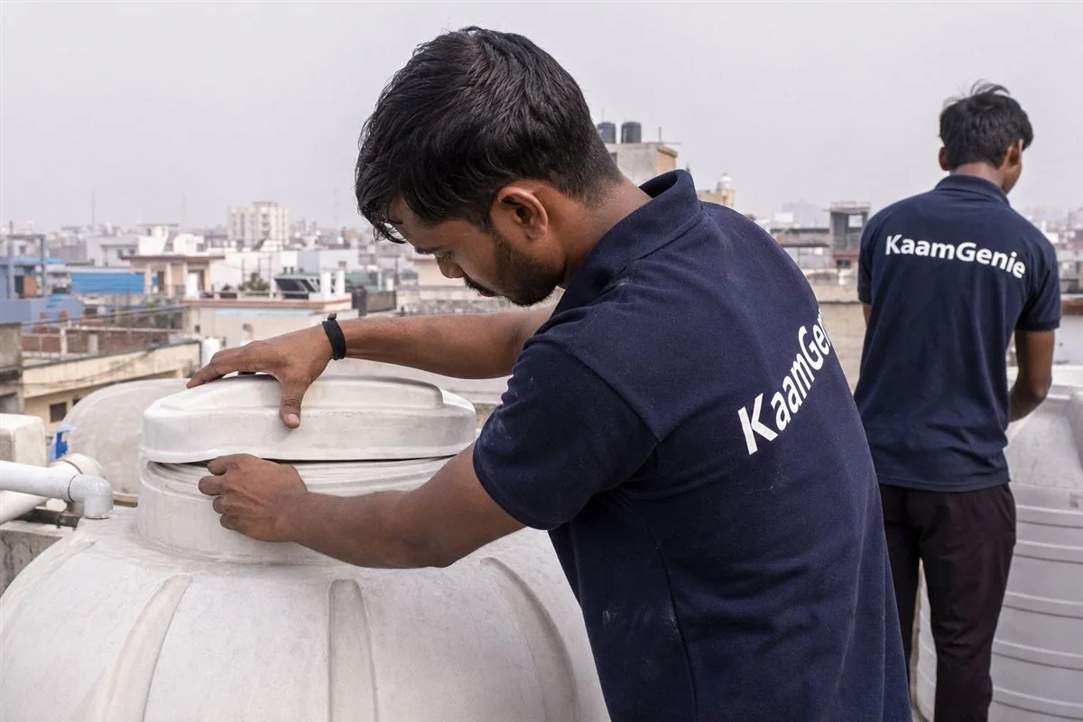 A KaamGenie worker in a navy shirt sealing a water tank lid tightly after cleaning on a Noida rooftop