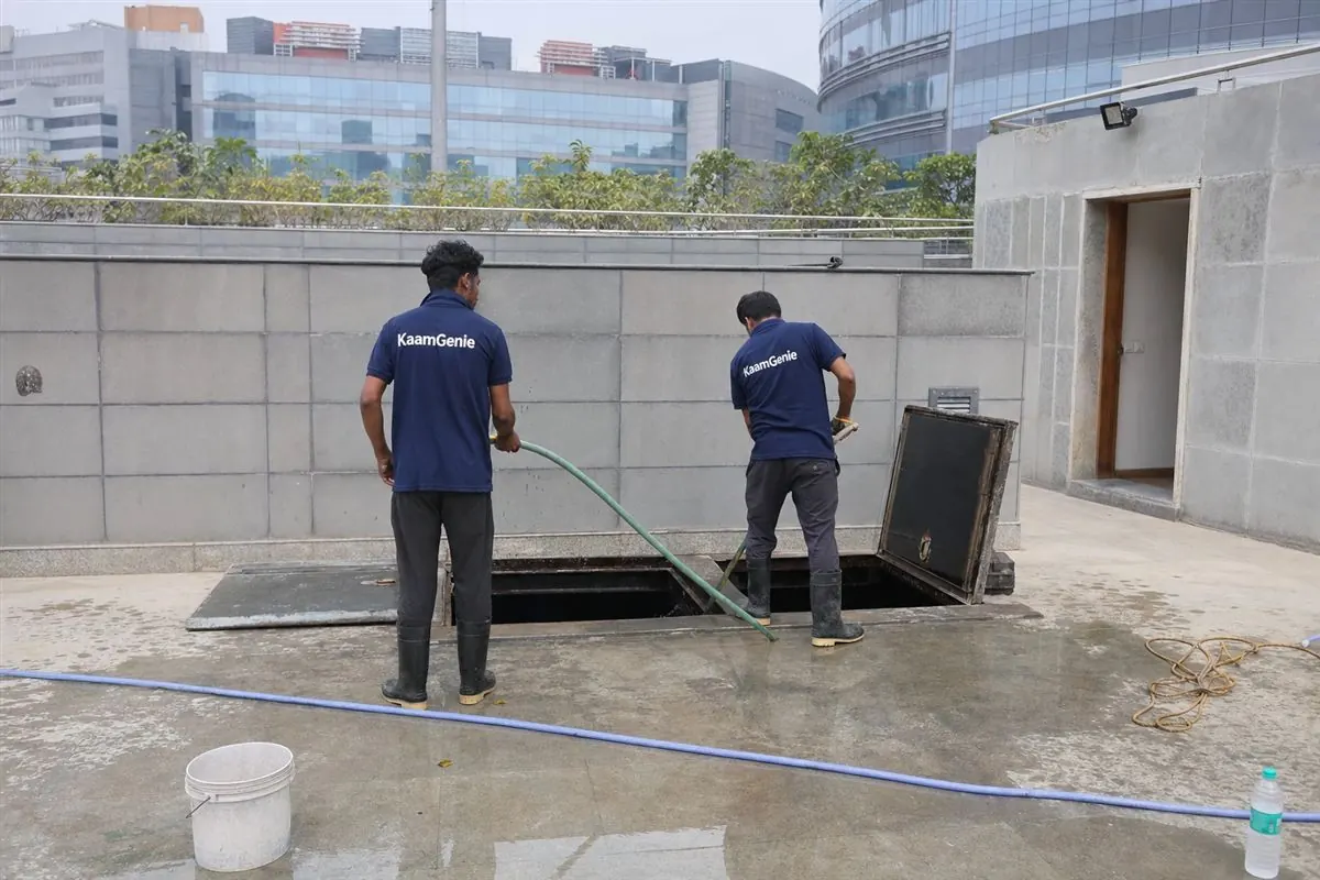 KaamGenie crew in navy shirts cleaning a large underground water reservoir at a Gurgaon corporate office tower in Cyber City