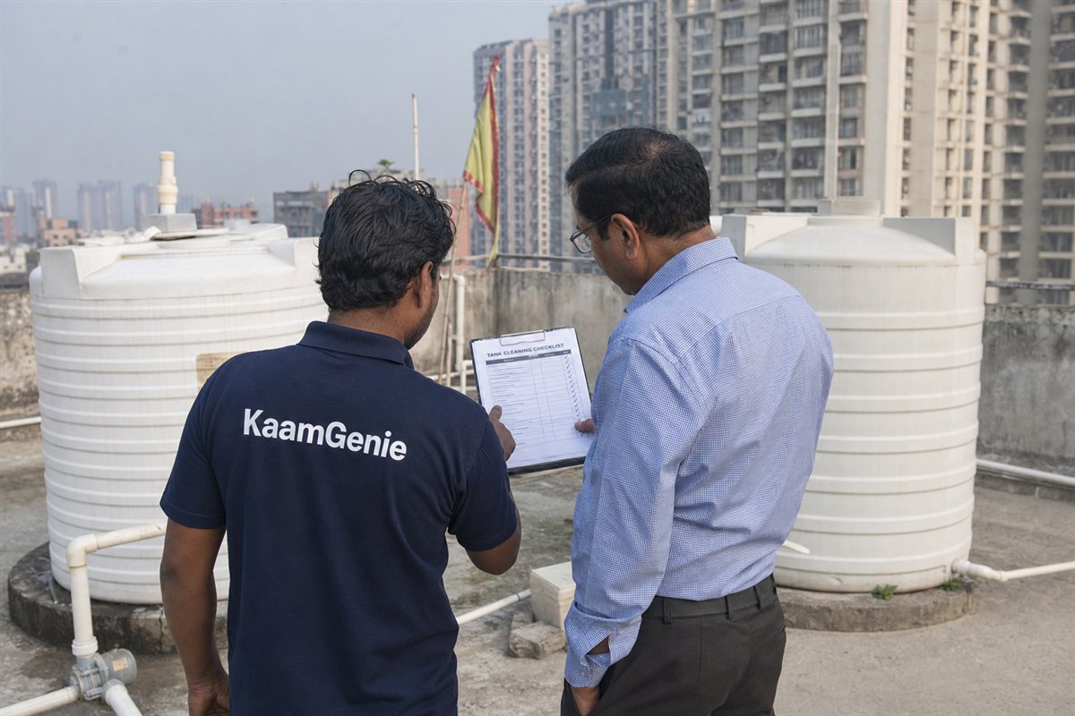 A KaamGenie worker in a navy shirt reviewing a tank cleaning checklist with a Gurgaon facility manager beside a corporate building reservoir
