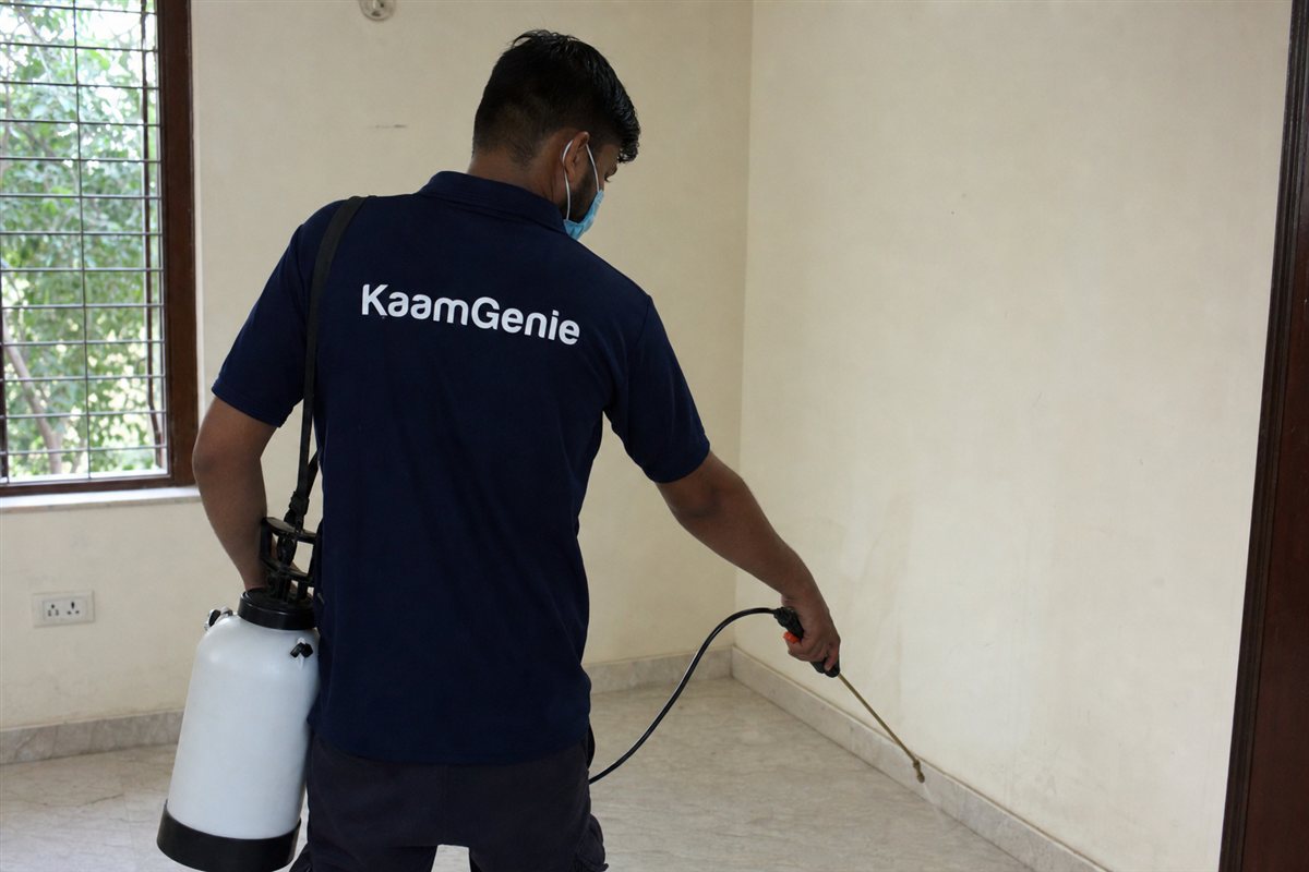 KaamGenie technician treating the skirting and empty kitchen cabinets of a bare Delhi flat before the family moves in