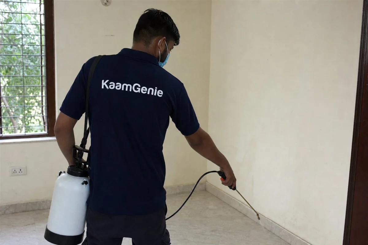 KaamGenie technician treating the skirting and empty kitchen cabinets of a bare Delhi flat before the family moves in