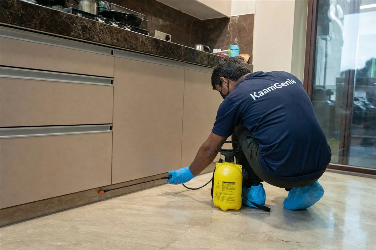 A trained KaamGenie technician in a navy branded shirt treating a Delhi kitchen with proper equipment during a local pest control booking
