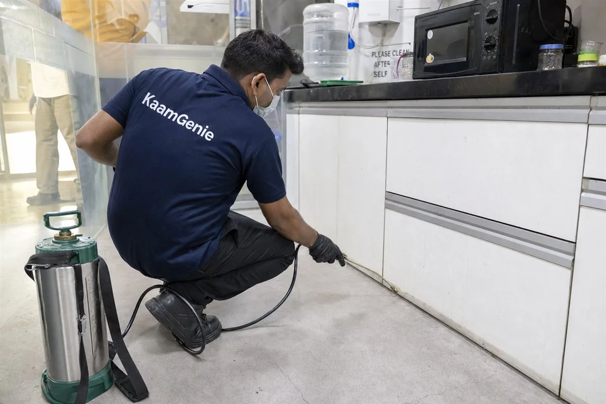 KaamGenie pest control technician carrying out a commercial cockroach and rodent treatment in an office pantry at Okhla Industrial Area Phase 2, South-East Delhi