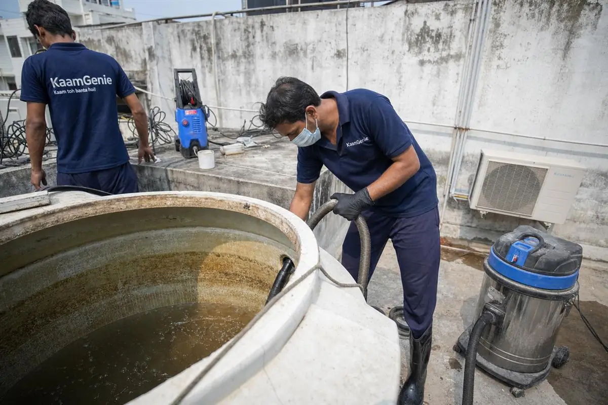 KaamGenie crew cleaning a large rooftop water tank at a Delhi PG accommodation building
